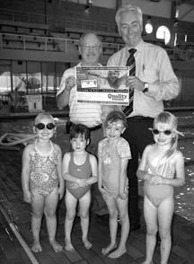 Rec bucks: Bill Reid from Parks & Rec and Bruce Robertson from Quality Foods, along with some young swimmers,introduce the Rec Bucks program.